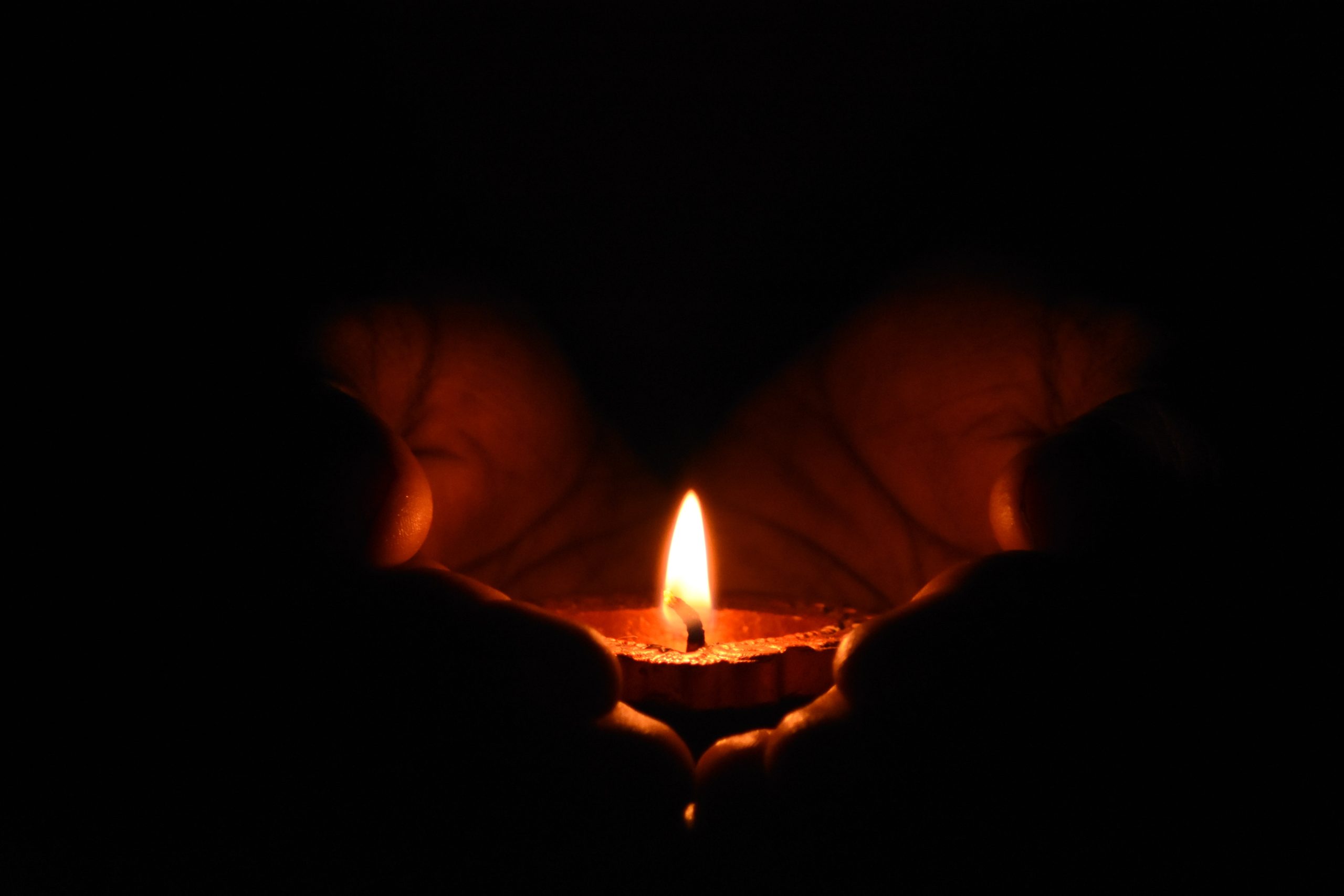 Two hands holding a small candle in the dark